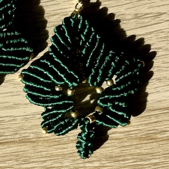Detail tmavě zelené macramé náušnice ve tvaru javorového listu s korálky ve zlaté barvě a ručně vázanými uzlíky.